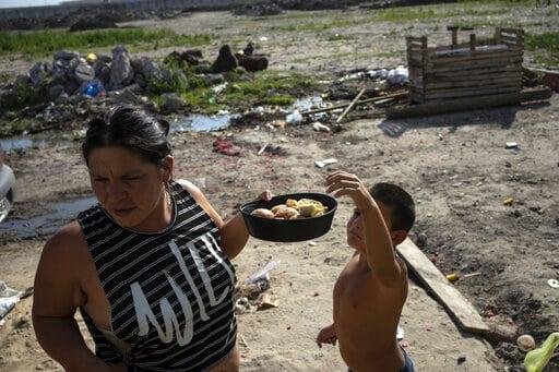 ARCHIVO - Andrea Calisti sostiene un molde de pan dulce donado mientras su hijo Nathanael de 7 años toma un pedazo, entregado por miembros de la organización social Movimiento de Trabajadores Excluidos en el barrio 17 de Octubre de Buenos Aires, Argentina, el 2 de febrero de 2022. (AP FOTO/RODRIGO ABD, ARCHIVO)