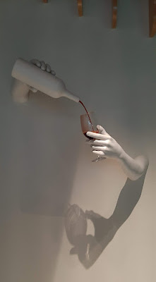 escultura de uma mão branca segurando um copo sendo servido de vinho de uma garrafa branca