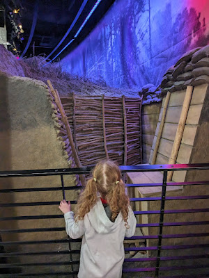 a girl with pigtails looks at a reproduction trench at the National WWI Museum