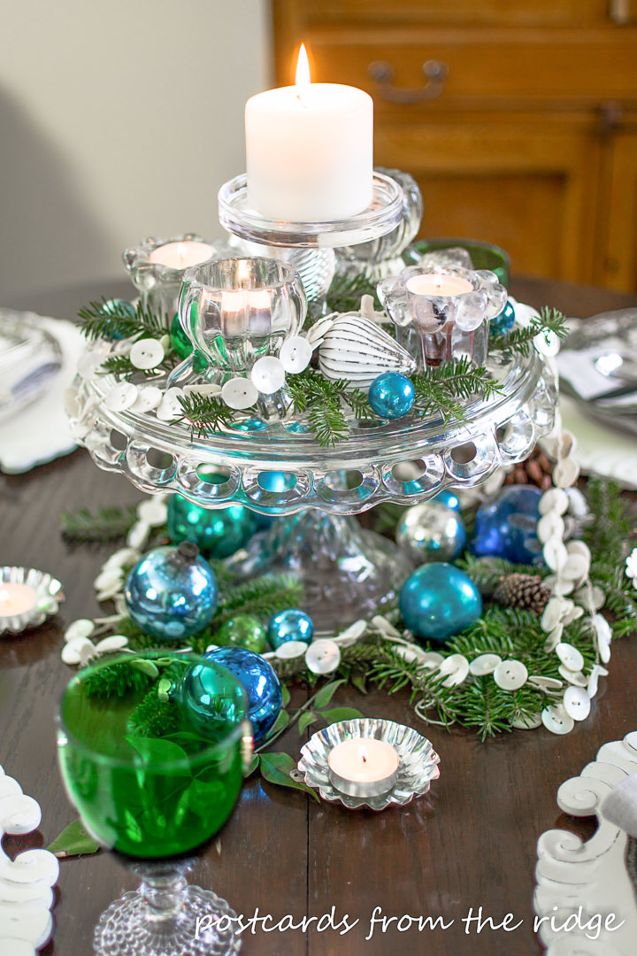 vintage glass cake pedestal with candles and glass ornaments as a Christmas table centerpiece