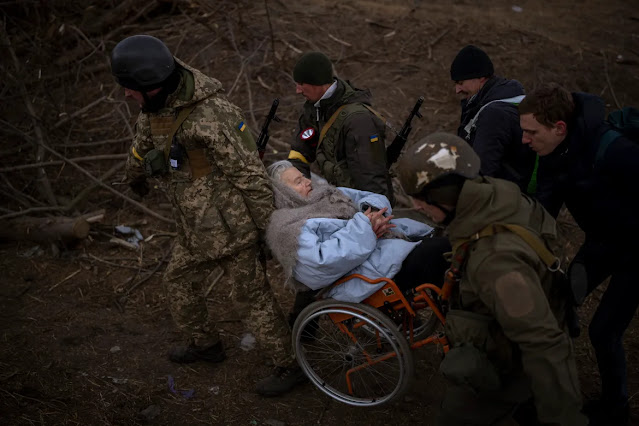 Ukrainian soldiers and militiamen carry a woman in a wheelchair in Irpin. [Emilio Morenatti/AP Photo]