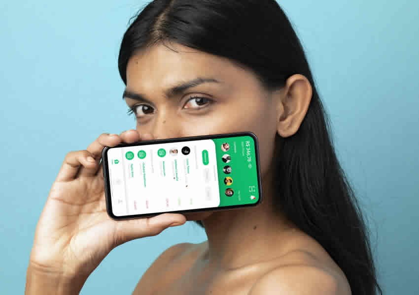 Imagem mostra uma mulher sobre um fundo azul claro segurando um smartphone inclinado perto de seu rosto mostrando o aplicativo do PicPay aberto.