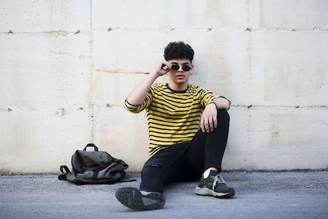 Ethnic young man with cool hairstyle sitting on asphalt