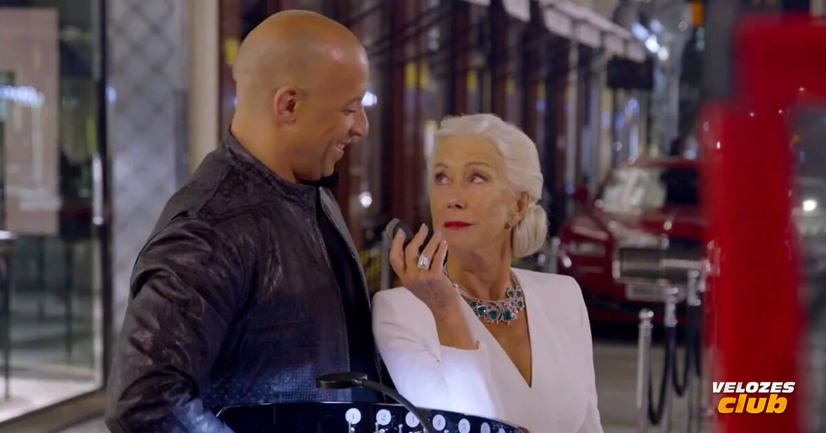 Na imagem vemos o ator Vin Diesel com a Atriz Helen Mirren, ele está com uma expressão positiva no rosto e também apontando um objeto para ele, ambos estão se olhando.