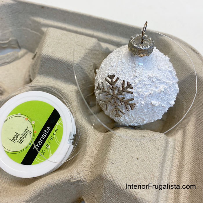 A small metal snowflake charm hung from clear craft thread onto recycled tree ornament hook.