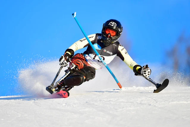 Forster contorna um obstáculo azul de um circuito de slalom. Ela usa um esqui adaptado com uma espécie de cadeira. A alemã veste uma malha amarela, capacete preto e um colete com o número 19