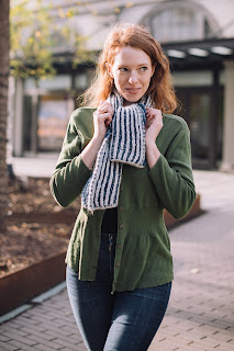 A woman wearing a bulky-knit reversible scarf. The scarf is knit in two-colour fisherman's ribbing, forming vertical stripes in two colours, off white and dark blue.