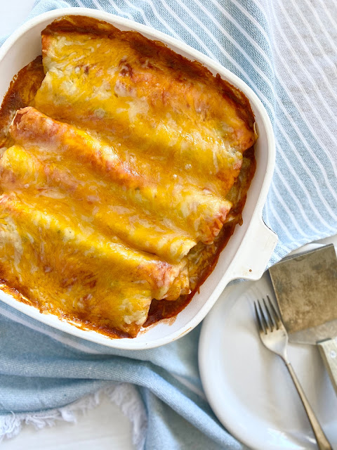 Casserole dish of beef burritos with plate, fork and spatula.