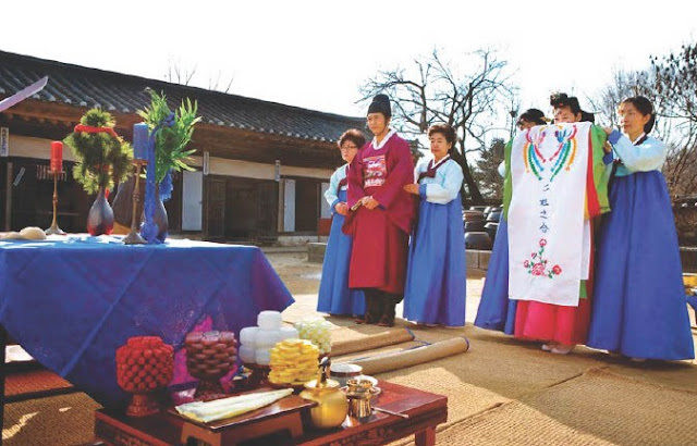 A Korean bride and groom in traditional wedding garments stand ready to be married.
