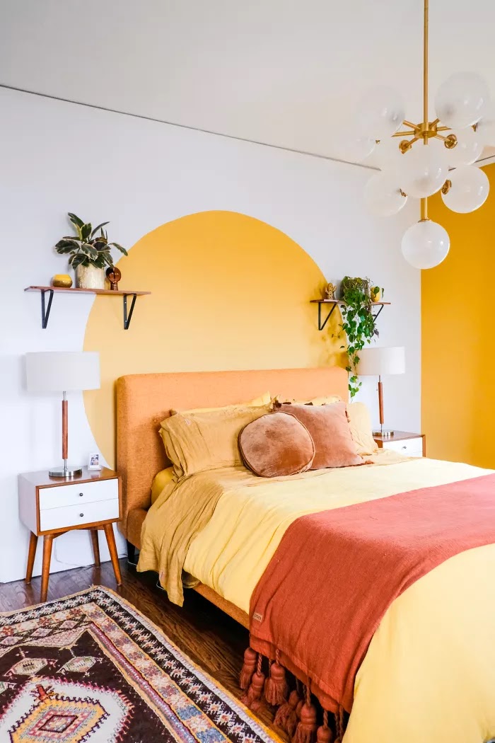 Duvarda parlak sarı bir daire, sarı bir yatak ve yatak takımı ve baloncuklu bir avize olan aydınlık ve neşeli bir yatak odası.