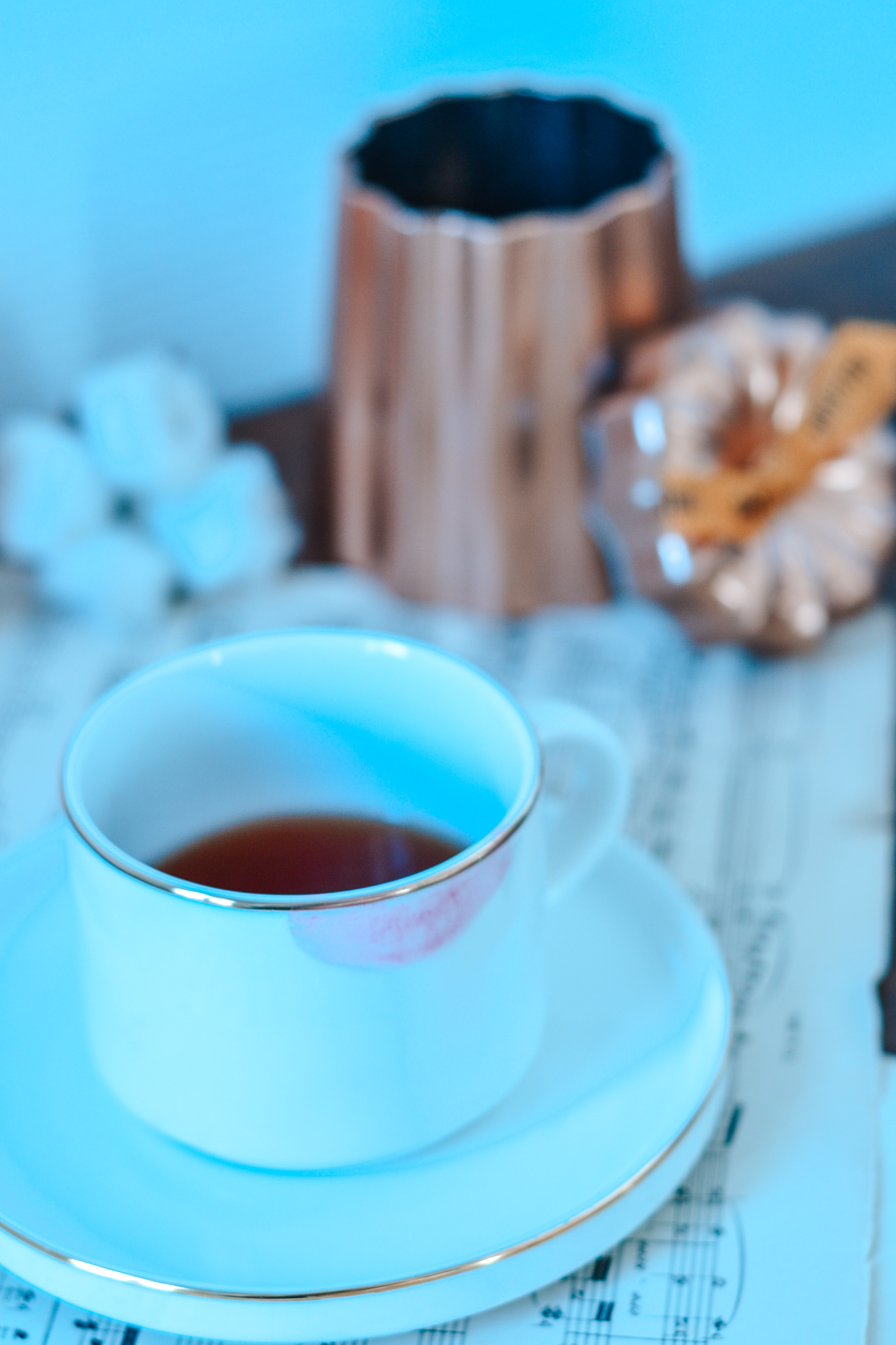 le thé au canelé de la marque chris'teas dans une tasse blanche et une boîte à thé en cuivre flouté au fond