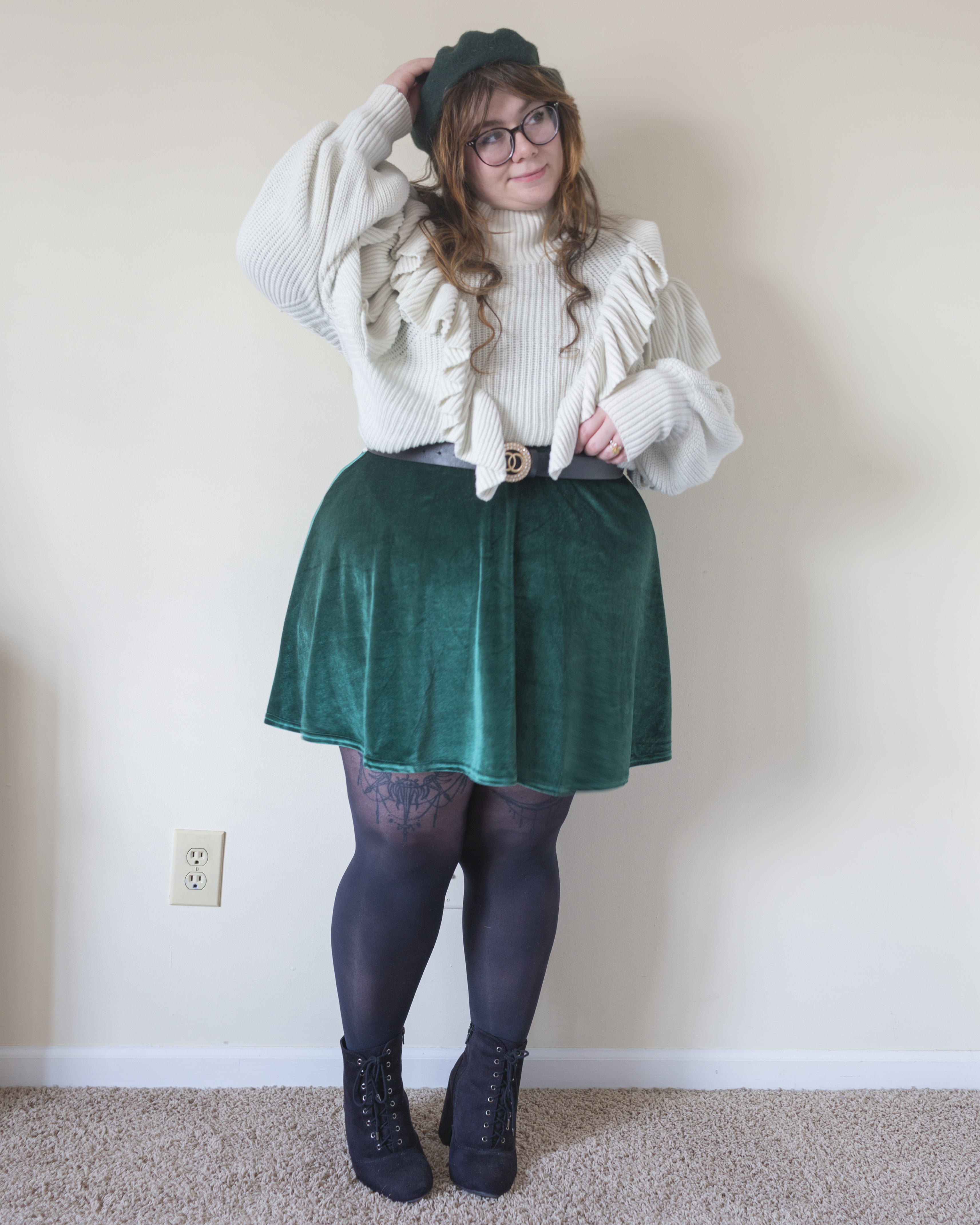 An outfit consisting of a dark green wool beret, white high neck sweater with bishop sleeves and ruffles on the bodice, tucked over a green velvet skater dress and black seude lace up block heel boots.