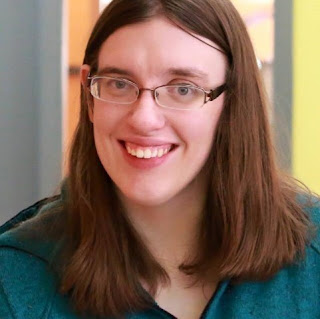 A woman with medium-length hair, glasses, wearing a green top