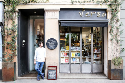 Immagine della vetrina di una libreria chiamata "Verso" con un libraio alla porta.