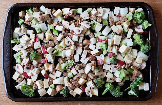 Mixed vegetables, vegan sausage, and tofu spread onto baking sheet to be put into oven.