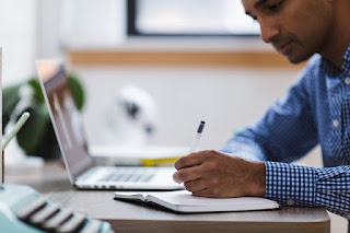 man writing notes on table beside laptop to complete assignment and avoid betrayal of trust