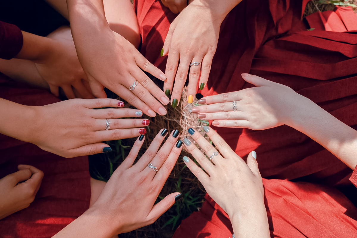 women with various bright manicures demonstrate each other their nails