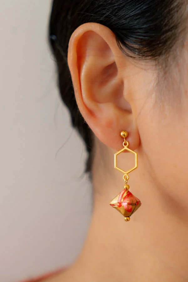 hexagonal golden, pink, and red patterned paper dangle earring displayed on model's earlobe