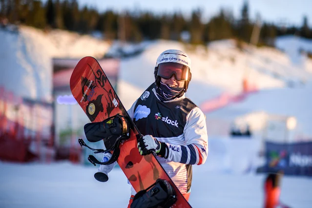 Montaggioni posa para foto segurando sua prancha vermelhar de snowboard. O fracês veste um casaco e capacetes brancos