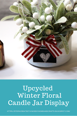 Pinterest pin showing faux winter floral inside of painted blue candle jar, with mini chalkboard and bow