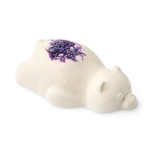 A white bear shaped bath bomb with a heart shaped bunch of purple lavender buds in the middle on a bright background