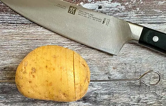 How to cut hasselback potatoes. It's actually easy, just insert a metal skewer as near to the bottom as you can, horizontally through the potato. Then using a sharp knife, slice the potato 5mm apart. The skewer will not allow the knife to go all the way through.
