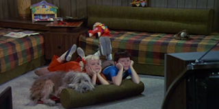 Cindy Brady, Bobby Brady, and Tiger watch the TV in the family room.