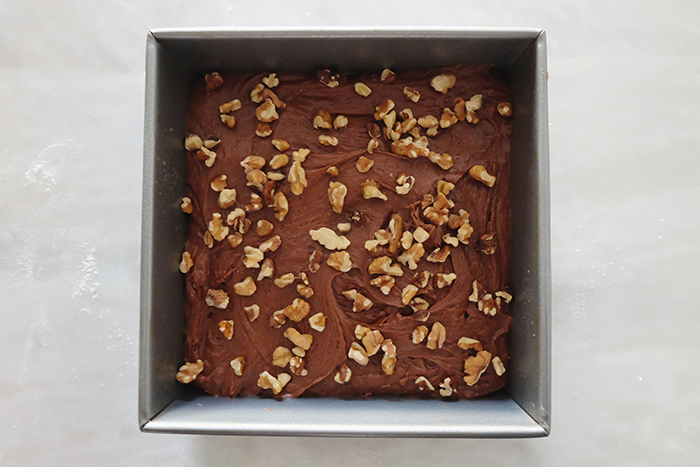 brownie batter in metal baking pan with walnuts atop