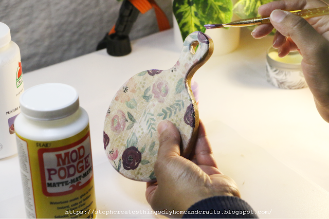 Hand holding paintbrush applying paint to round wood riser