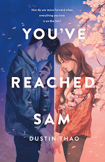 A teenage boy in a jean jacket in blue lighting on the left, a teenage girl in a pink jacket on the right. The boy is under dark blue lighting and the girl is under a pink sky and cherry tree. Their hands clasp across the dividing line as they hold their phones in their free hands.