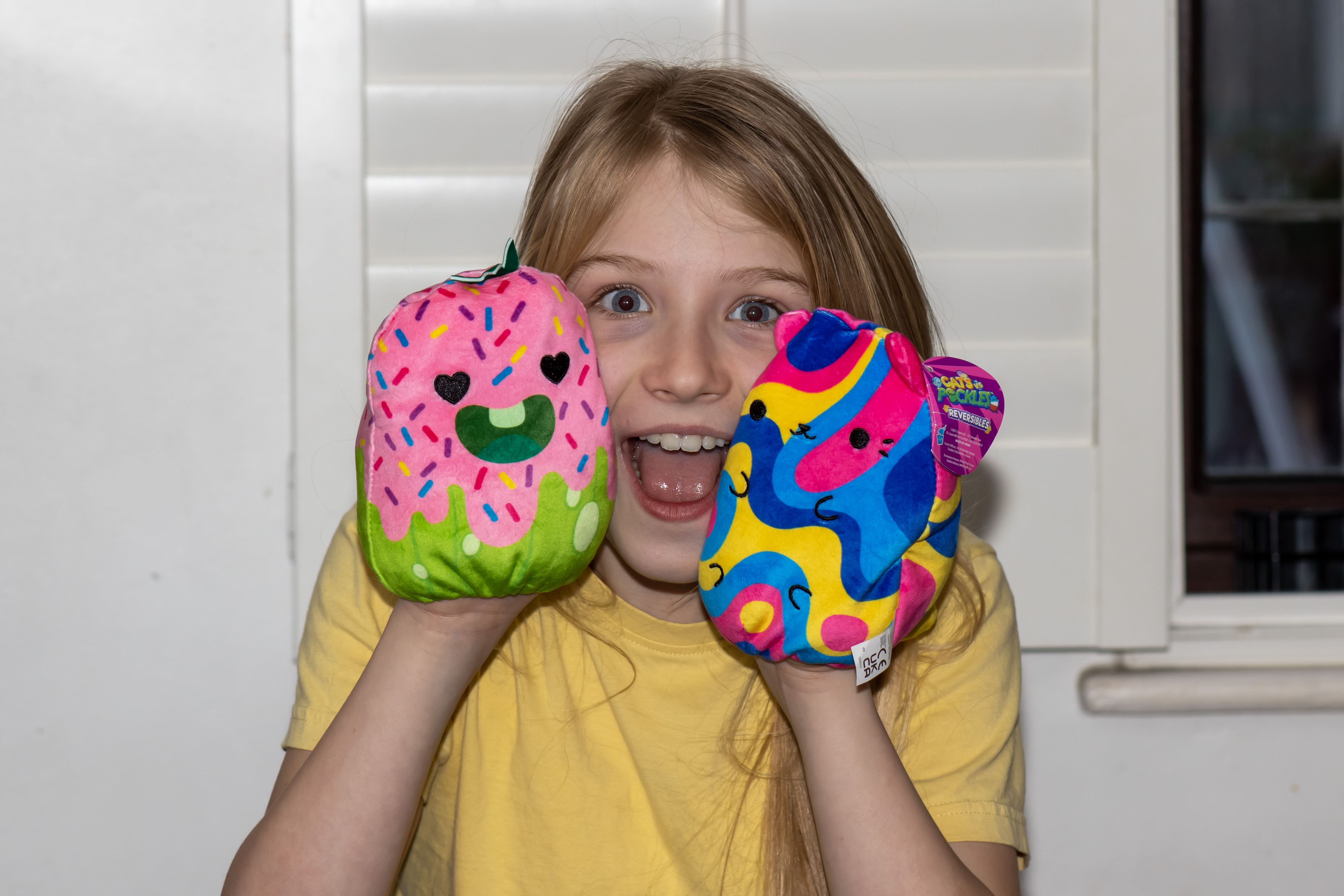 A tween girl in a yellow top playing with cats versus pickles reversible plush toys received for review