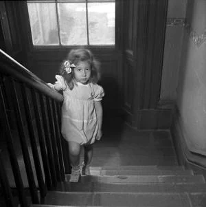 black and white photograph of young girls on stairway with window behind her, NYC c. 1946