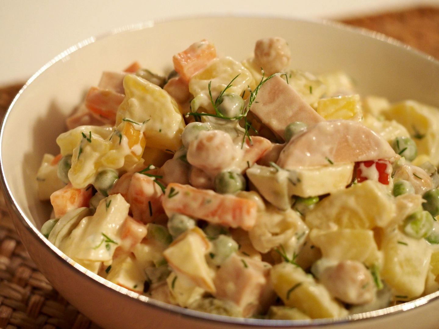 Eine Schüssel mit einem reichhaltigem Salat aus Kartoffeln, Karotten, Erbsen, Kichererbsen, veganer Fleischwurst und sauren Gurken.
