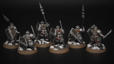 Heavily armoured dwarf warrior miniatures from the back in front of a black background.
