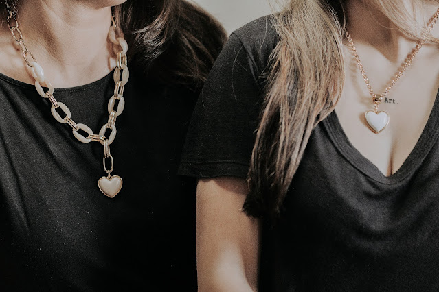 Two friends wearing black tops and pendant necklaces.