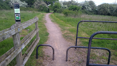 A gravel path off into fields partially blocked by steel hoops you have to step round/ over.