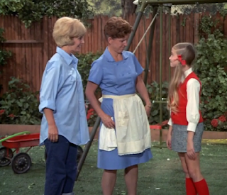 Marcia tells Alice and Carol her good news in the Brady backyard.