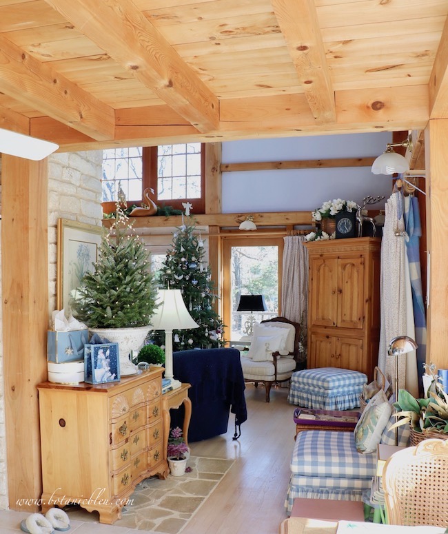 Both the French country tabletop starry tree and large angel-decorated tree in the living room are visible while seated at the sunspace breakfast table.