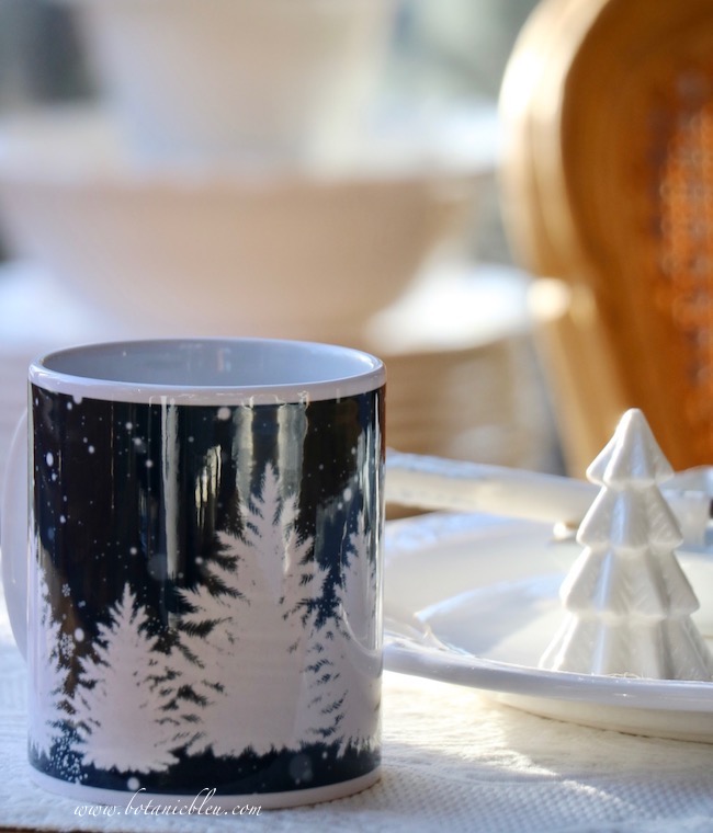 Snowy trees of varying heights cover the a Winter mug on all sides