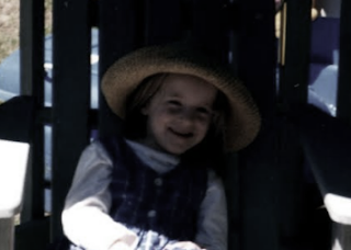 K at about 5 years old. She is smiling and wearing a straw hat.