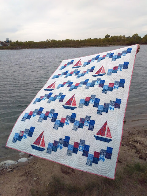 Patchwork quilt made of blue and red fabrics on a light background. combination of sailboat blocks and squares  arranged in a wave pattern.