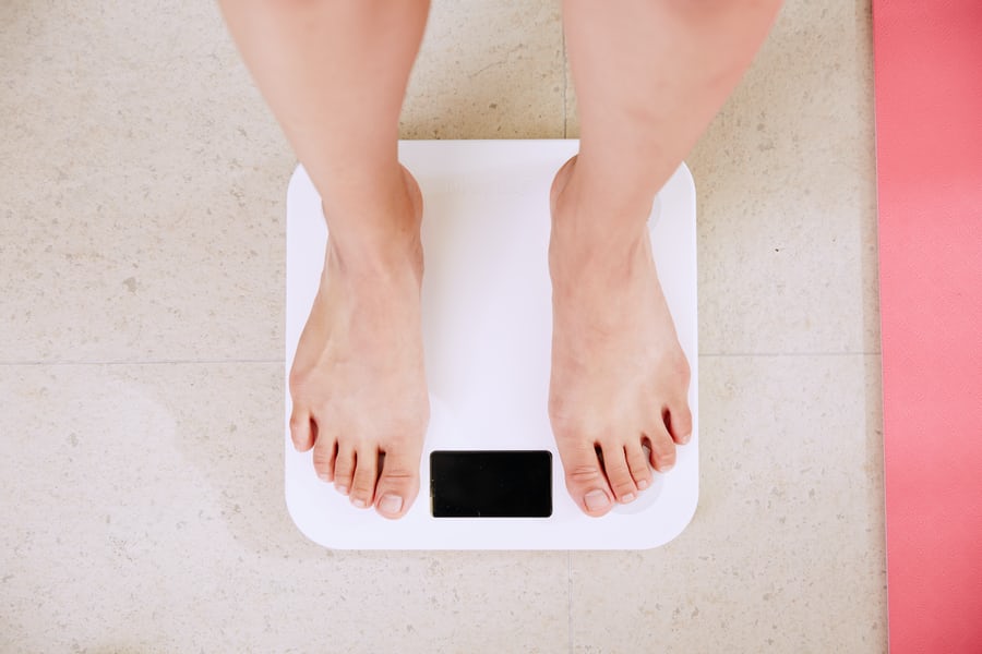 Two feets of a white woman measuring her weight on a weight loss scale