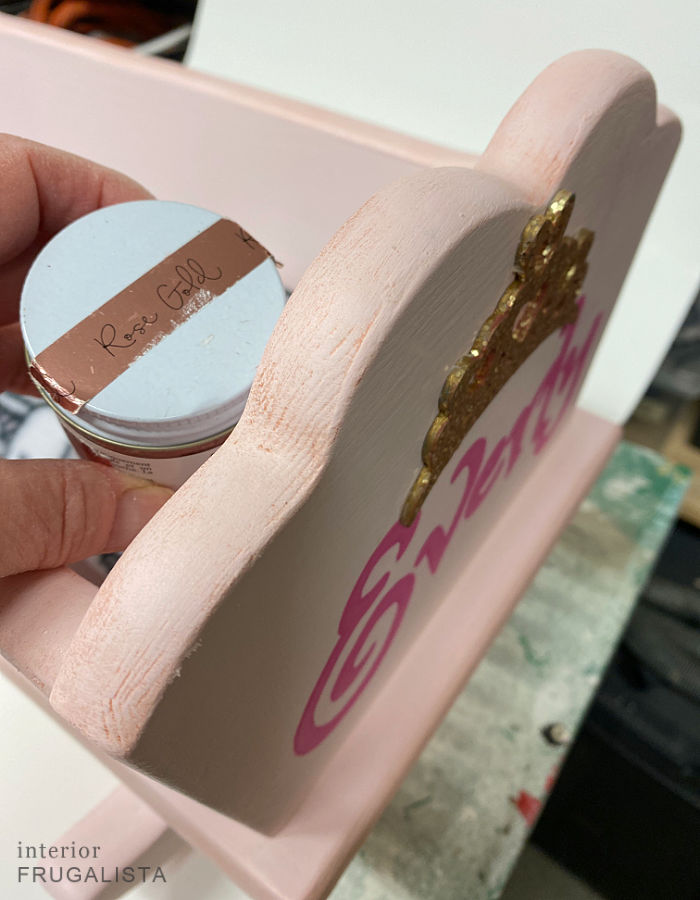 Applying rose gold highlights on a wooden doll cradle makeover with furniture wax.