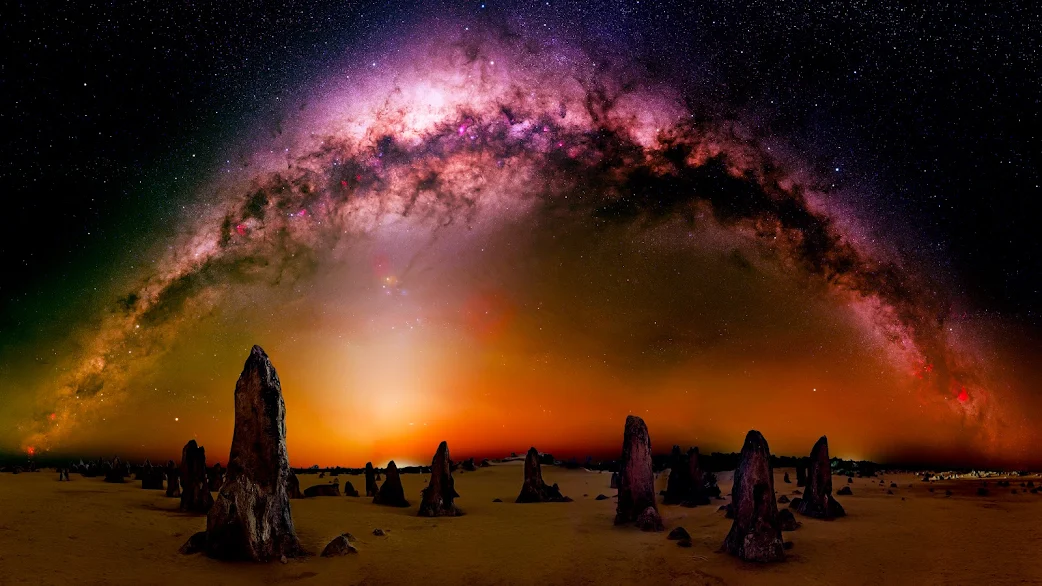 Sweeping view of the Milky Way over ancient rock formations in a desert captured in 4K, ideal for an awe-inspiring PC wallpaper