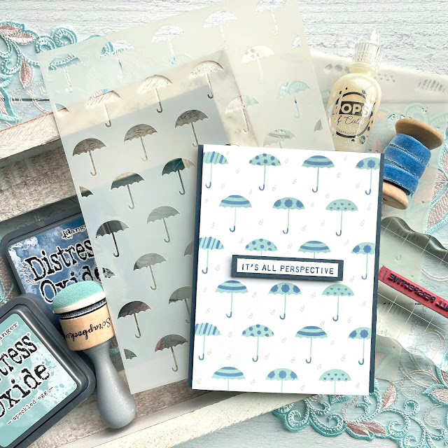 Rainy Day card made with : Scrapbook.com umbrellas stencil, pops of color snowflake, domed foam blending tool; Tim Holtz distress oxide speckled egg and faded jeans, tiny text stamp