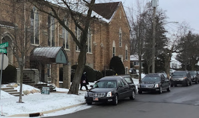 line of black funeral cars parked at church entrance