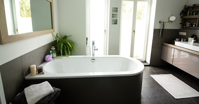 Freestanding bathtub in a large bathroom with a plant in the corner.