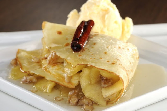 descrição: na foto se vê um tipo de sobremesa que é um  crepe de maçã caramelizado, decorado com canela em casca e acompanhado com sorvete.