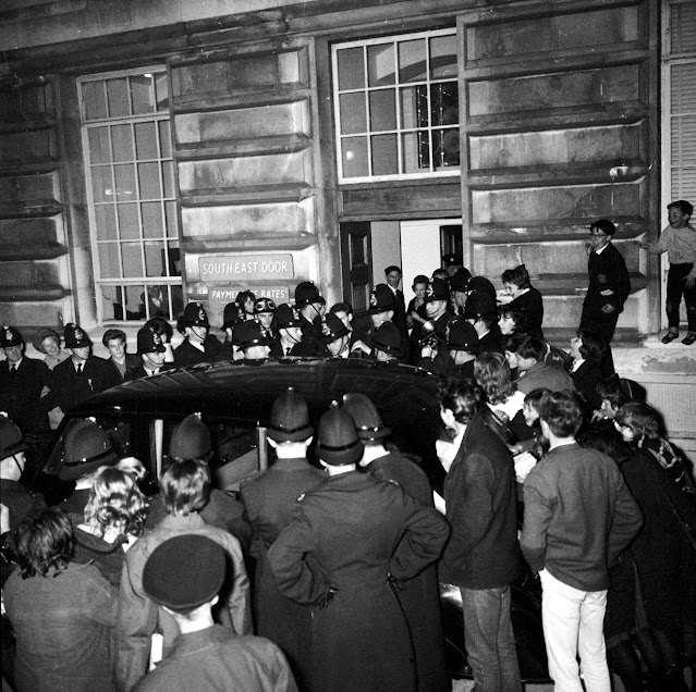 Los fanáticos de los Beatles ven cómo los policías escoltan al grupo hasta su automóvil