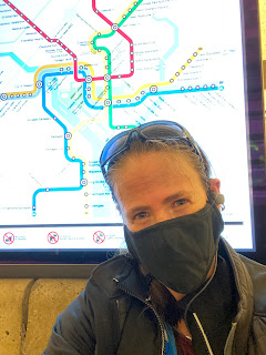 Selfie of me in a mask sitting in front of a Metro map in the Smithsonian station.